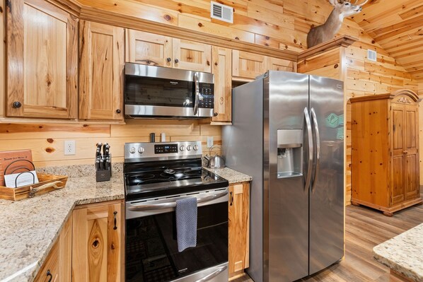 A kitchen with wooden cabinetry, stainless steel appliances including a microwave, oven, and refrigerator, and a wooden deer head decoration on the wall. - Beside Still Water 2 - 2 Bedrooms, 2 Baths, Sleeps 6 Home by RedAwning (Cosby)