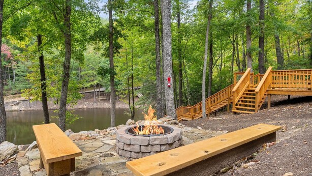 A fire pit surrounded by stone benches in a forested area with a wooden bridge and a pond. - Beside Still Water 2 - 2 Bedrooms, 2 Baths, Sleeps 6 Home by RedAwning (Cosby)