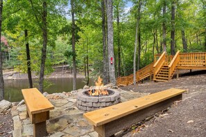 A fire pit surrounded by stone benches in a forested area with a wooden bridge and a pond. - Beside Still Water 2 - 2 Bedrooms, 2 Baths, Sleeps 6 Home by RedAwning (Cosby)