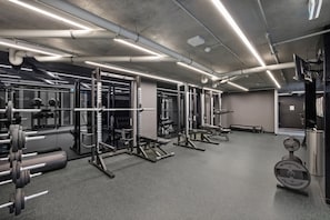 A gym with weightlifting equipment, mirrors, and a grey carpeted floor.