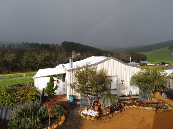 A white building with a sloped roof, surrounded by a garden with various plants and a pile of firewood. - Moonlight Studio- Nannup's favourite accommodation. (Nannup)