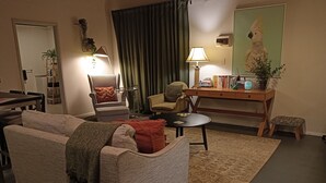 A living room with a sofa, armchairs, a coffee table, a small table with books, a lamp, and a painting of a bird.