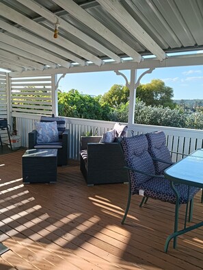 A covered outdoor seating area with wooden flooring, cushioned seating, and a table. - Moonlight Studio- Nannup's favourite accommodation. (Nannup)