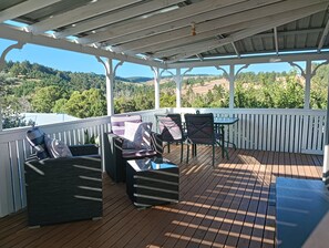 A covered outdoor seating area with wooden flooring and white railings, featuring cushioned chairs and a small table. - Moonlight Studio- Nannup's favourite accommodation. (Nannup)