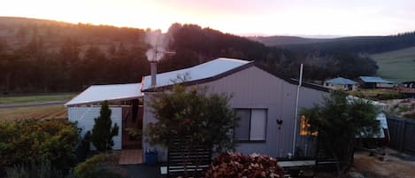 A rural property with a large building, a stack of firewood, and a clear view of the surrounding landscape.