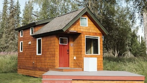 Eine kleine Holzhütte mit roter Tür, zwei Fenstern und einer kleinen Veranda.