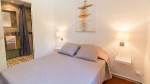 A hotel room with a bed, two bedside lamps, a wall-mounted artwork, and a bathroom visible through an open door. - Le Mas, Provencal house between sea and vineyards (Hyères)