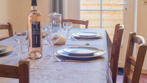 A dining table set with plates, glasses, and a bottle of wine, with a view of a wooden deck outside. - Le Mas, Provencal house between sea and vineyards (Hyères)