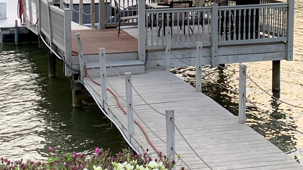 Een houten steiger die leidt naar een tuinhuisje met een metalen dak, omgeven door water en huizen op de achtergrond.