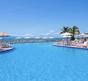 A pool area with lounge chairs and umbrellas, a clear sky, and a view of the ocean.