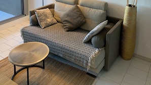 A modern living room with a sofa, a coffee table, a floor lamp, a framed picture, and a tall vase with pampas grass.