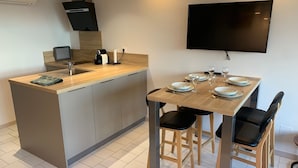 A modern kitchen with a central island, a dining table with four chairs, and a flat-screen TV mounted on the wall.