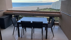 A balcony with a table and chairs, overlooking a beach and a distant building.