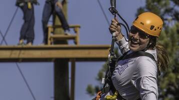 A woman in a harness and helmet suspended on a zip line.
