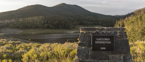 A stone sign with the text "Gaylord Reservoir 1992" in a natural landscape with mountains and grass.