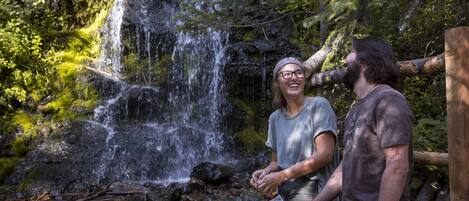 A couple sitting by a waterfall in a forested area.