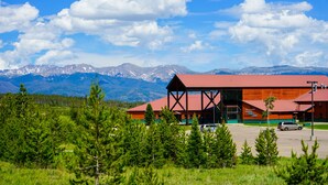 A lodge with a red roof and wooden structure, surrounded by green trees and mountains in the background. - YMCA of the Rockies Snow Mountain Ranch (Granby)