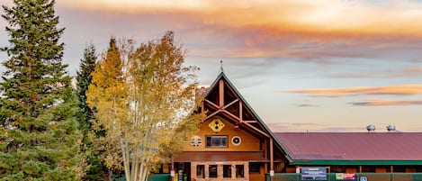A lodge with a red roof and a stone facade, surrounded by trees and a parking lot.