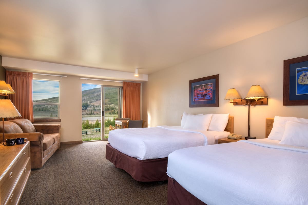 A hotel room with two beds, a desk, a chair, and a view of the outdoors.