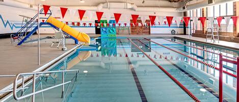 A large indoor swimming pool with multiple lanes, a water slide, and a lifeguard station.