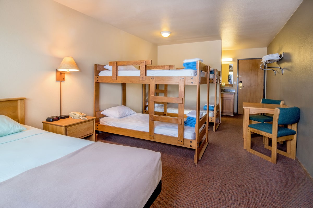 A hotel room with bunk beds, a desk, a chair, a nightstand with a phone, and a lamp.