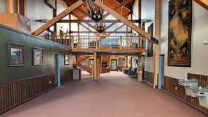 A spacious interior with a high ceiling, wooden beams, a central staircase, and a view of the outdoors. - YMCA of the Rockies Snow Mountain Ranch (Granby)