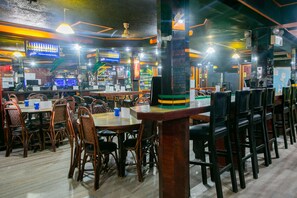 A restaurant with wooden tables and chairs, a bar area, and a television screen displaying a menu. - OYO 722 Slouch Hat Inn (Manila)