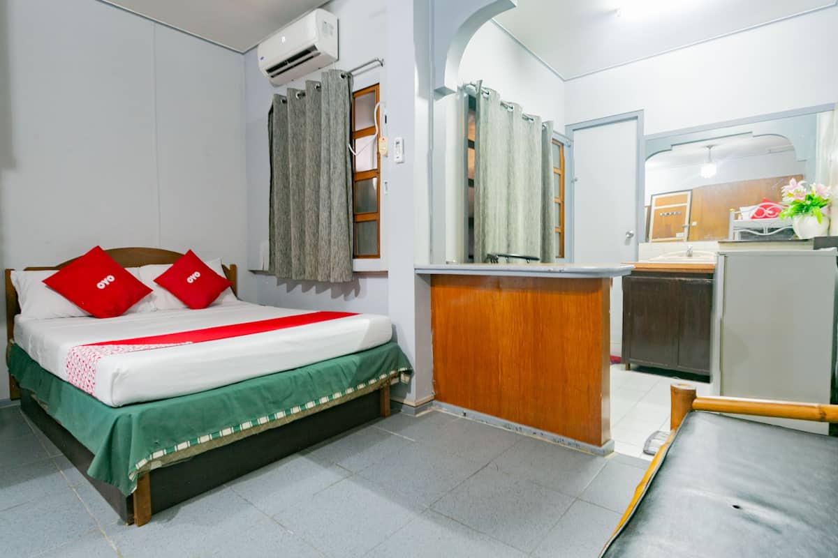 A compact hotel room with a bed, a small kitchenette, a bathroom, and a shower area.