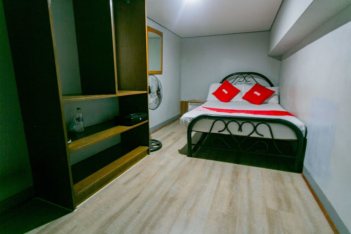 A bedroom with a bed, a wardrobe, a mirror, and a fan.