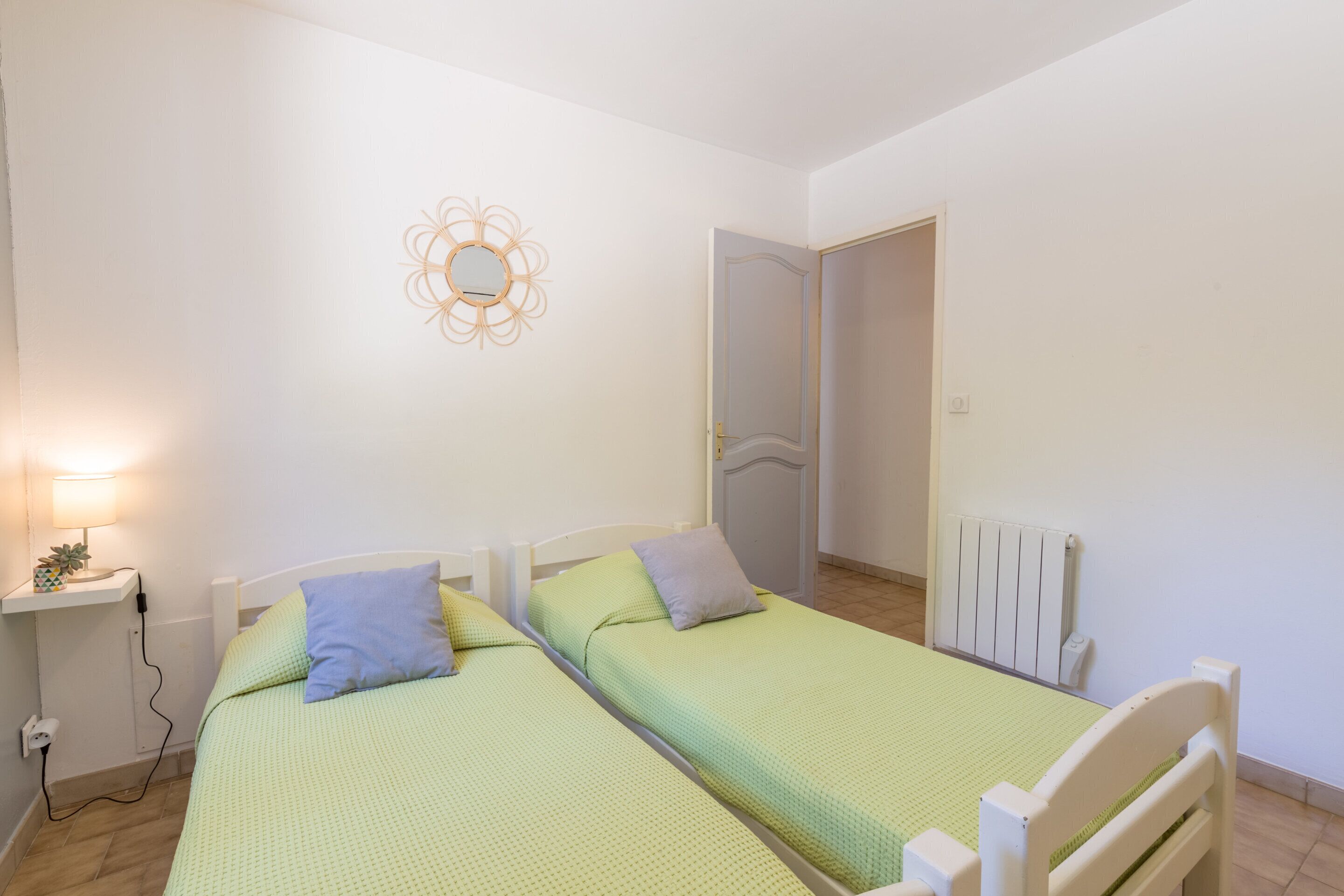 A bedroom with two single beds, a bedside table with a lamp, a wall decoration, and a radiator.
