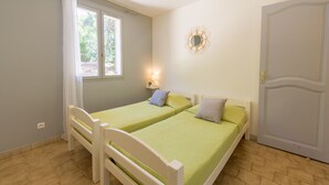Ein kleines, helles Schlafzimmer mit zwei Einzelbetten, einem Fenster mit Vorhängen, einem an der Wand befestigten Spiegel und einer Tür.