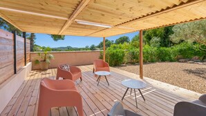 Eine Holzterrasse mit Gartenmöbeln, einer Pergola und Blick auf Grünflächen und Hügel.