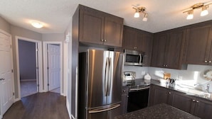 A modern kitchen with stainless steel appliances, dark wooden cabinets, and granite countertops.