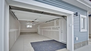 A garage with a closed door, a dark mat at the entrance, and a light-colored floor.