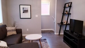 A living room with a sofa, a round coffee table, a TV on a stand, and a bookshelf.