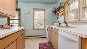 A kitchen with wooden cabinets, a white countertop, a built-in oven, and a window with a view of trees. -  Clara's Cottage, On Lake Michigan (Oostburg)