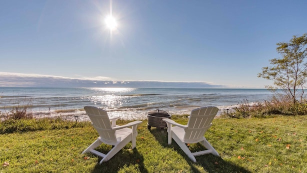 Two Adirondack chairs facing a body of water with a clear sky and a sun shining. -  Clara's Cottage, On Lake Michigan (Oostburg)