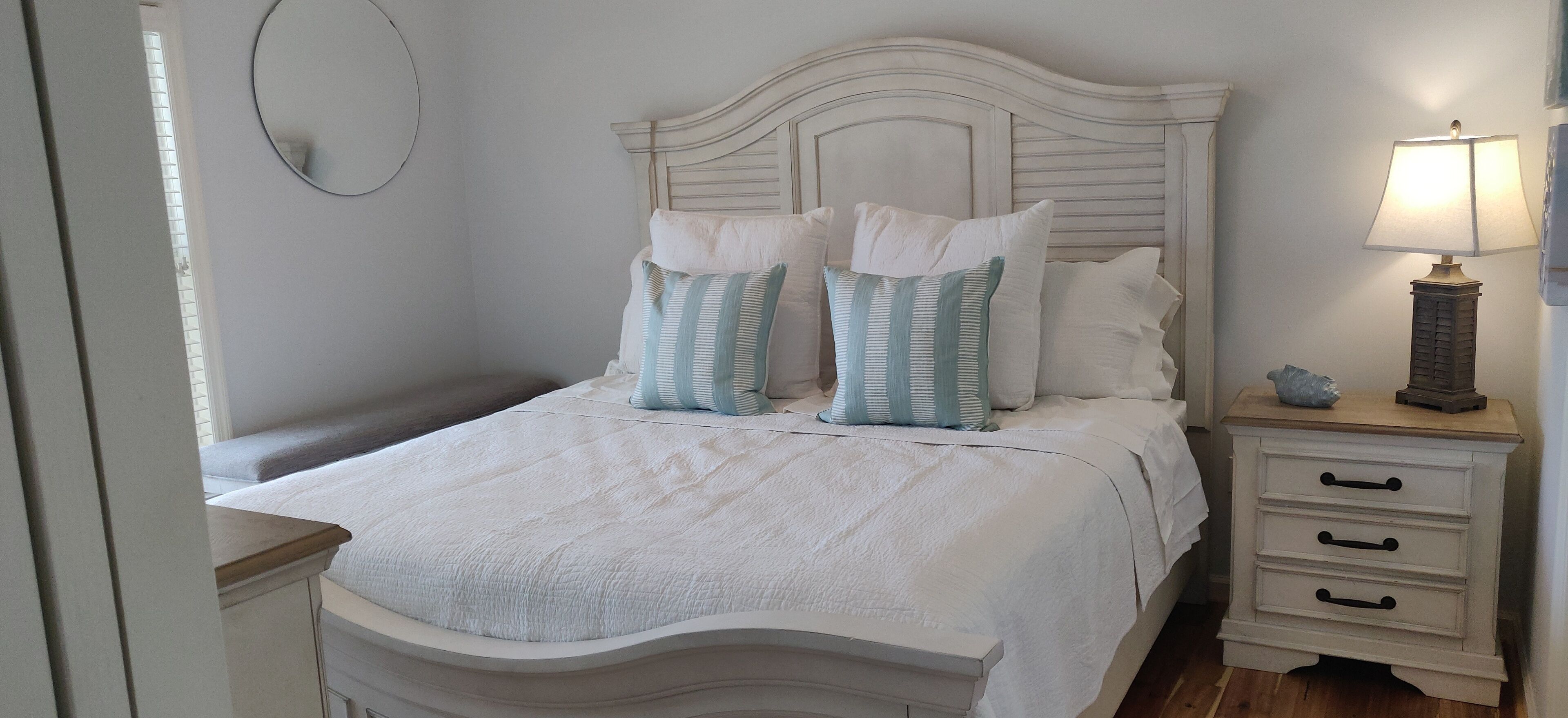 A bedroom with a bed, white bedding, two pillows, a bedside table with a lamp, and a nightstand.