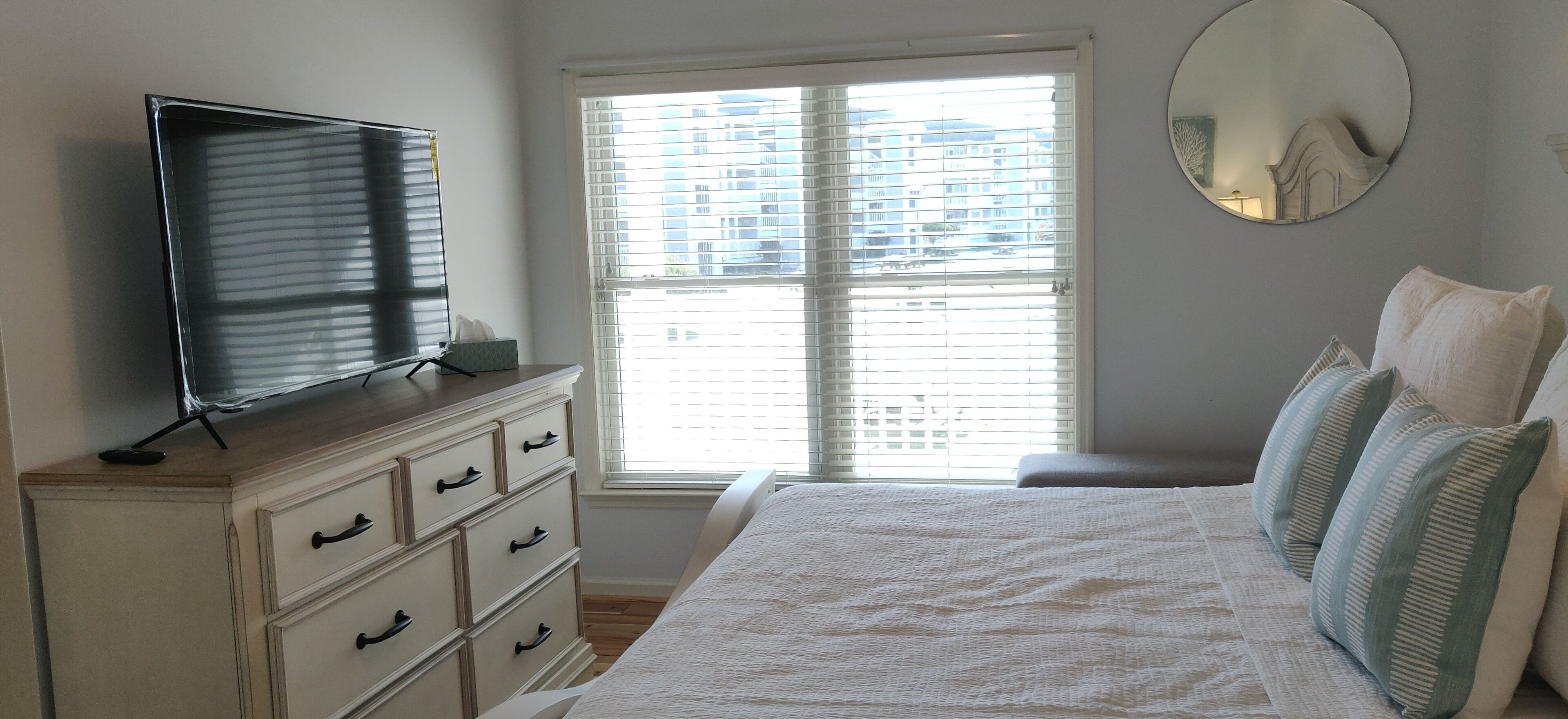 Een slaapkamer met een bed, een dressoir, een televisie en een raam met zonwering.