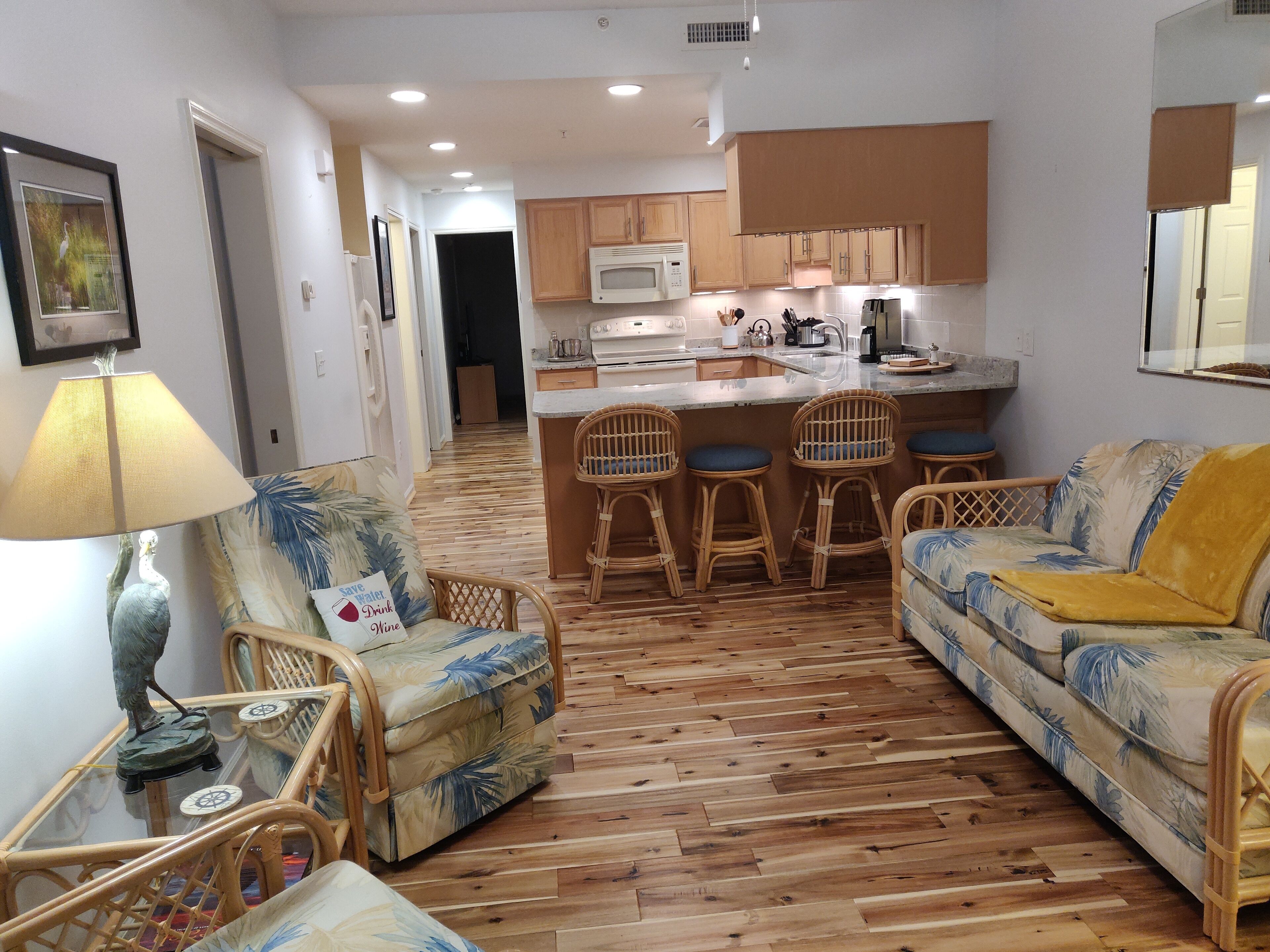 A compact living space with a kitchenette, a dining area with wicker chairs, and a sofa with a yellow throw.