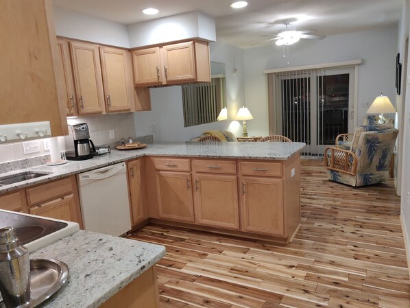 A kitchen with wooden cabinets, a granite countertop, a coffee maker, and a dining area with a chair and table.