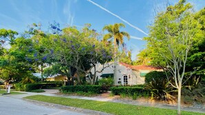 A residential area with a house featuring a white facade, green roof, and a small garden with various plants and trees. - Luxury Villa near Siesta - private, heated screened pool (Sarasota)