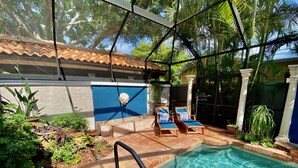 A pool area with a clear blue pool, surrounded by potted plants and two lounge chairs. - Luxury Villa near Siesta - private, heated screened pool (Sarasota)