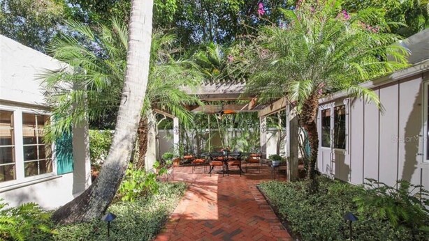 A brick pathway leading to a covered outdoor seating area surrounded by lush greenery and palm trees. - Luxury Villa near Siesta - private, heated screened pool (Sarasota)