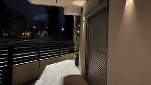 A nighttime corridor with a closed shutter door, a tiled floor, and a railing. - Lemon Tree Suites Near ATH Airport (Markopoulo Mesogaias)