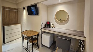 A compact room with a wooden table and chairs, a small kitchenette, a television, and a round mirror. - Lemon Tree Suites Near ATH Airport (Markopoulo Mesogaias)