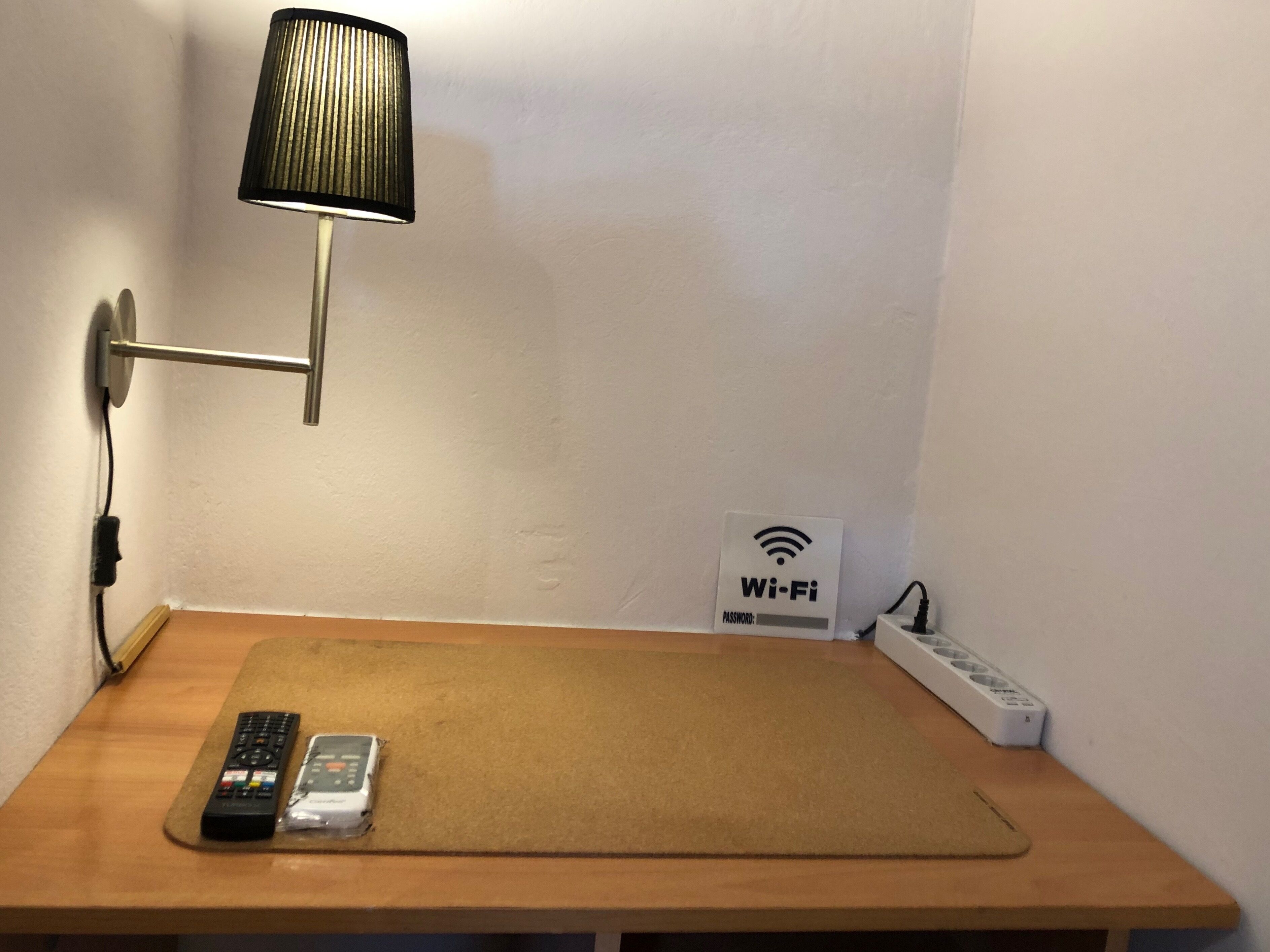Una pequeña mesa con una lámpara, un control remoto y un cartel de Wi-Fi.