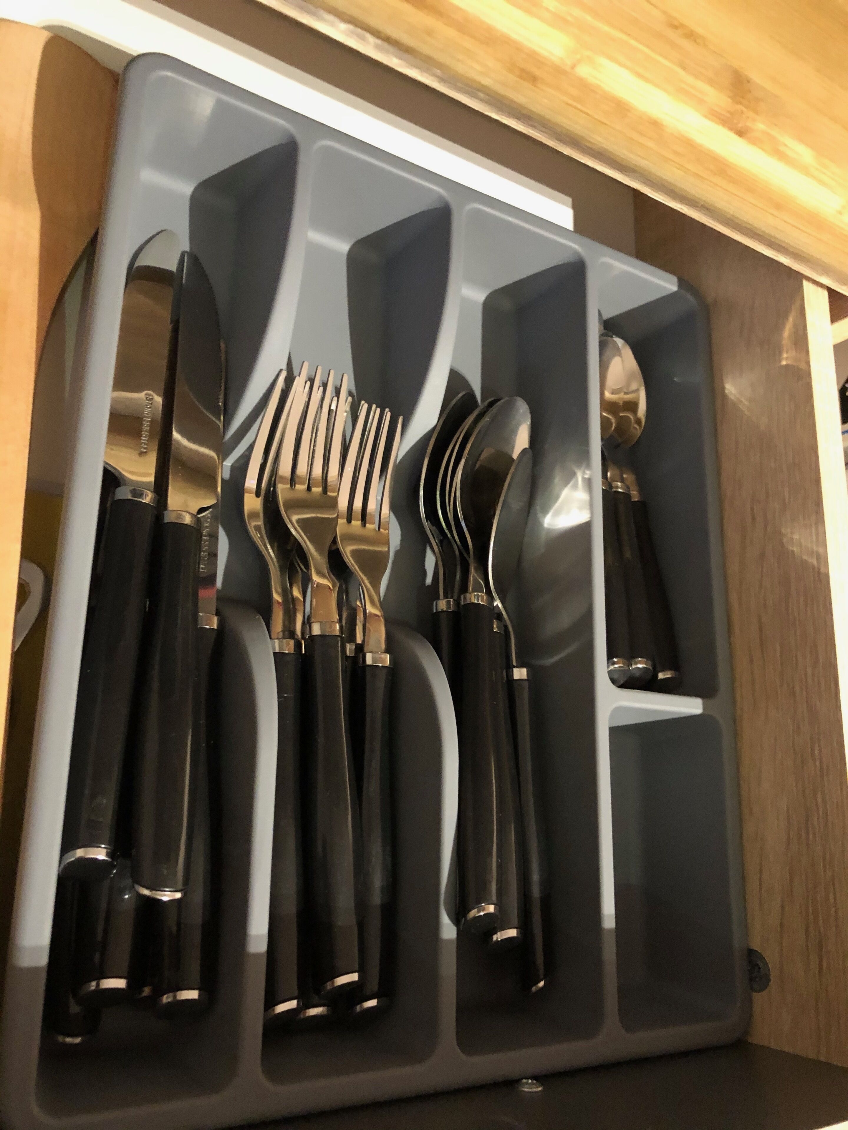 Een lade met een set zwarte bestekstukken, inclusief vorken, messen en lepels.