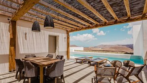 A terrace with a wooden table and chairs, a pool, and a view of the landscape. - One Bedroom Suite, Amarelo Suites (Mykonos)