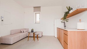 A compact living space with a kitchenette, a sofa, a small round table, and a window. - One Bedroom Suite, Amarelo Suites (Mykonos)